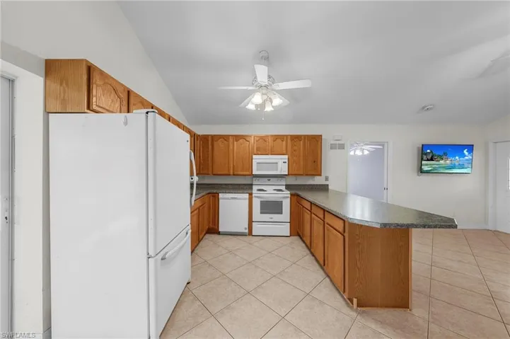 Kitchen featuring white appliances, brown cabinets, a peninsula, light tile patterned floors, and lofted ceiling