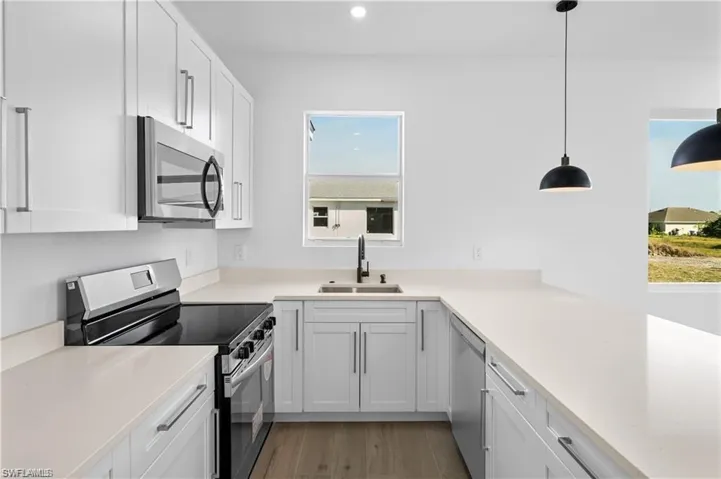Kitchen with stainless steel appliances, decorative light fixtures, sink, and white cabinets