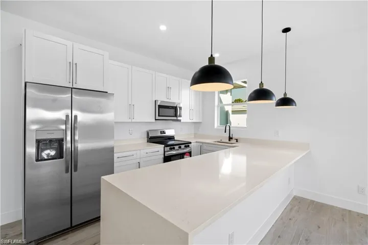 Kitchen with sink, appliances with stainless steel finishes, hanging light fixtures, white cabinets, and light wood-type flooring