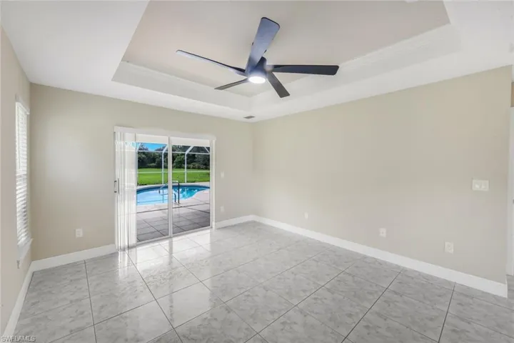 Recessed tray ceiling with a ceiling fan, sliding glass doors, pool access, and tiled flooring