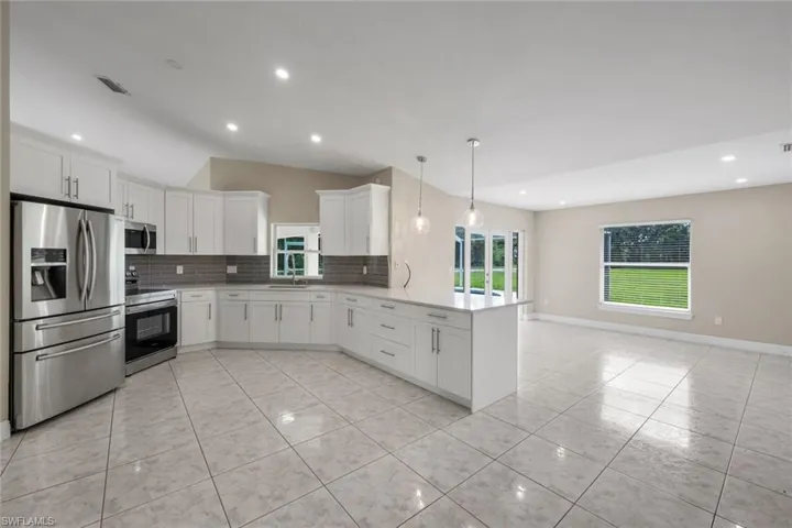Open-concept kitchen featuring white cabinetry, stainless steel appliances, a center island with pendant lighting, and tile flooring