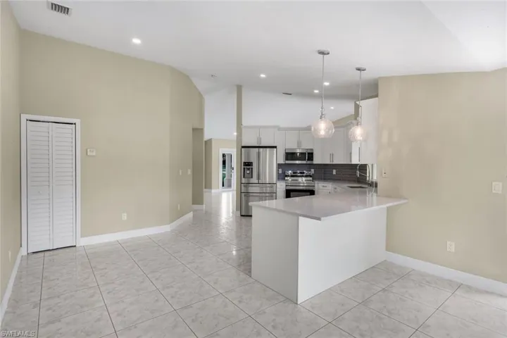 Open-concept living space featuring tiled flooring, vaulted ceilings, a kitchen island with seating, stainless steel appliances, and white cabinetry