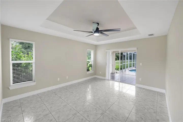 Spacious room featuring a tray ceiling, ceiling fan, and large windows