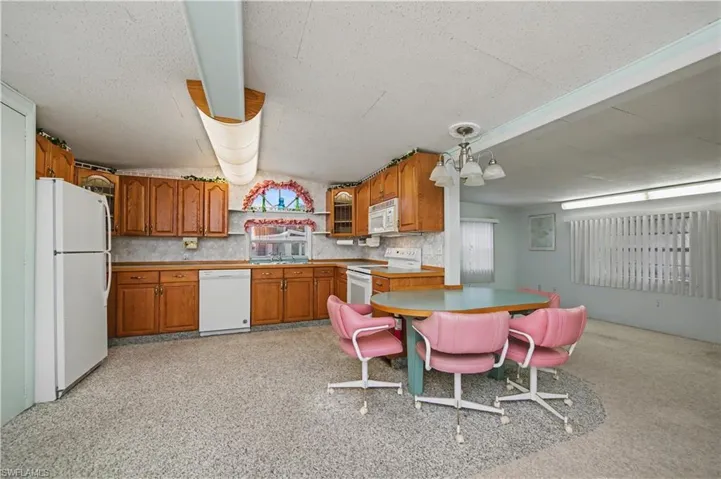 Kitchen with brown cabinets, white appliances, light countertops, lofted ceiling, and tasteful backsplash