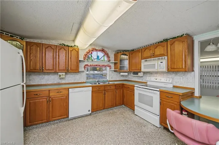 Kitchen featuring white appliances, brown cabinets, open shelves, light countertops, and tasteful backsplash