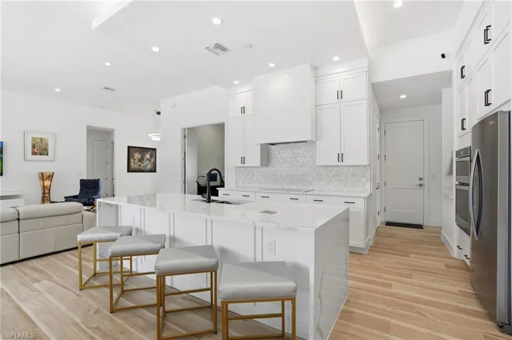 Kitchen with open floor plan, a kitchen bar, light stone counters, stainless steel appliances, and a kitchen island with sink