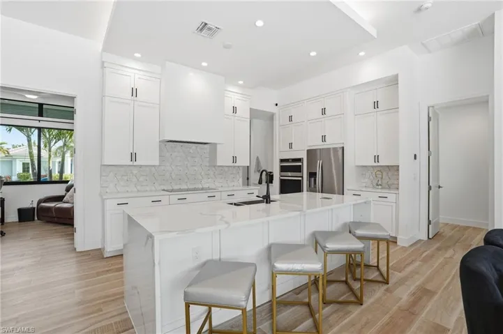 Kitchen featuring decorative backsplash, light stone counters, a kitchen breakfast bar, white cabinetry, and stainless steel appliances