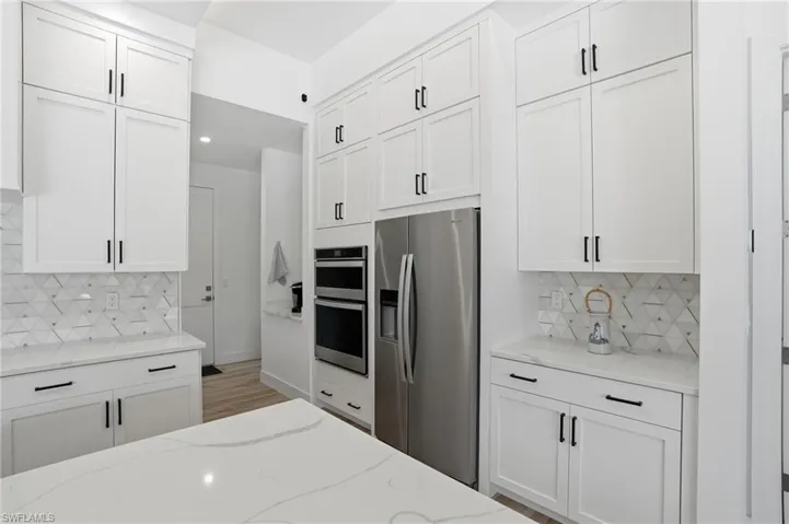 Kitchen with backsplash, stainless steel appliances, light stone countertops, and white cabinetry