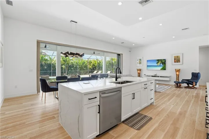 Kitchen with a sunroom, light stone countertops, an island with sink, white cabinets, and dishwasher