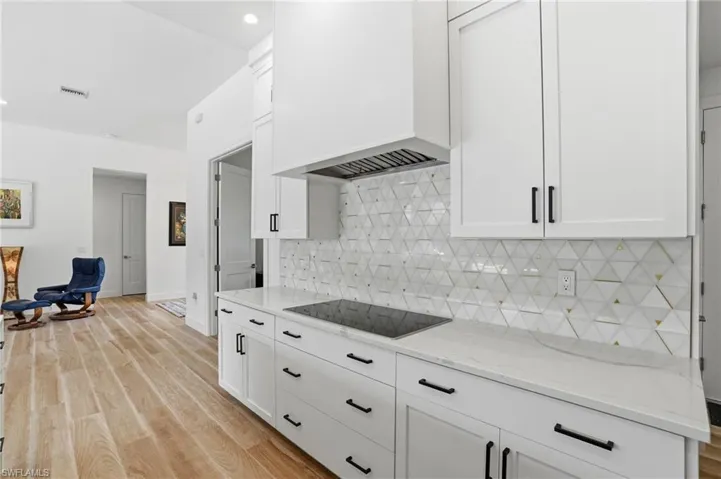 Kitchen featuring light wood-style floors, white cabinetry, light stone countertops, black electric stovetop, and recessed lighting