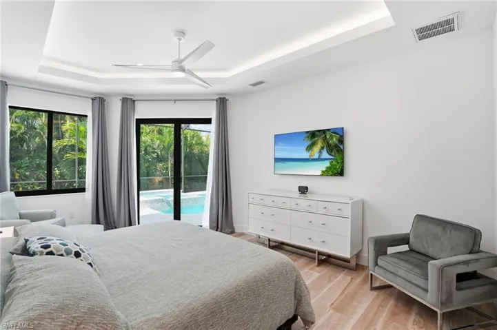 Bedroom featuring light wood-style flooring, access to exterior, a raised ceiling, and ceiling fan