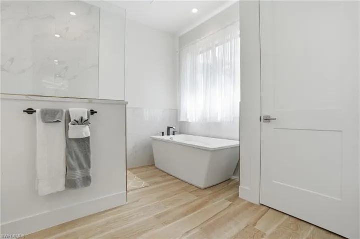 Bathroom with light wood-style flooring, a freestanding bath, recessed lighting, walk in shower, and wainscoting