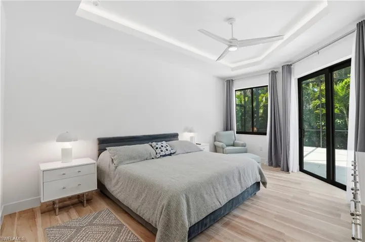 Bedroom with light wood-style flooring, a tray ceiling, access to outside, and ceiling fan
