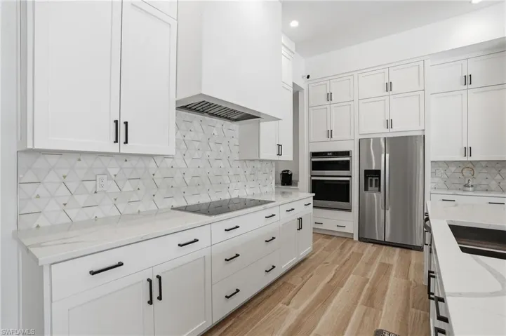 Kitchen featuring stainless steel appliances, white cabinetry, light stone counters, and recessed lighting