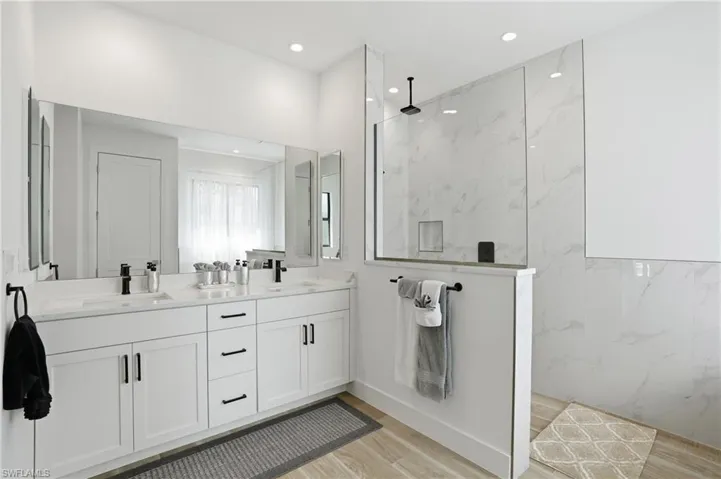 Full bath with double vanity, a marble finish shower, light wood-type flooring, and recessed lighting