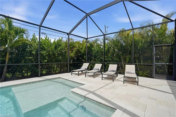 Outdoor pool featuring glass enclosure, a sunroom, a patio area, and a hot tub