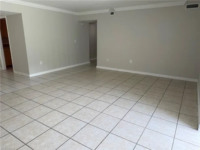 Spacious room featuring light-toned square tile flooring, neutral wall paint, white baseboards, and crown molding