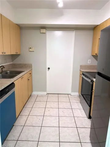 Galley kitchen featuring light wood-finish cabinetry, light-toned countertops, a tile backsplash, stainless steel sink, and tile flooring