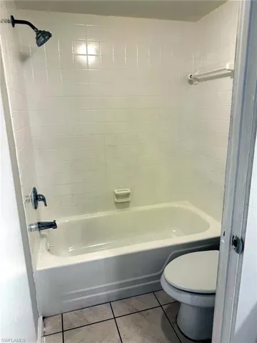 Bathroom featuring a white tub, shower with dark-finish fixtures, white subway tile surround, and square tile flooring