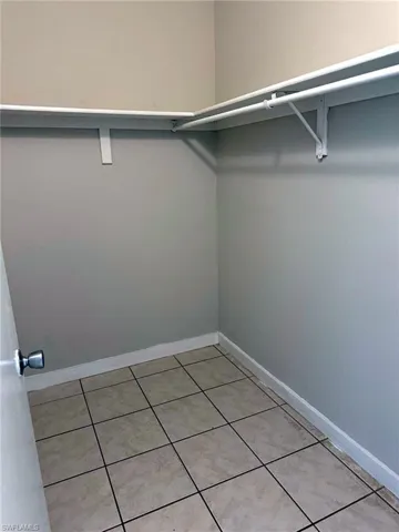 Spacious closet featuring light-toned walls, tile flooring, and integrated shelving with hanging rods