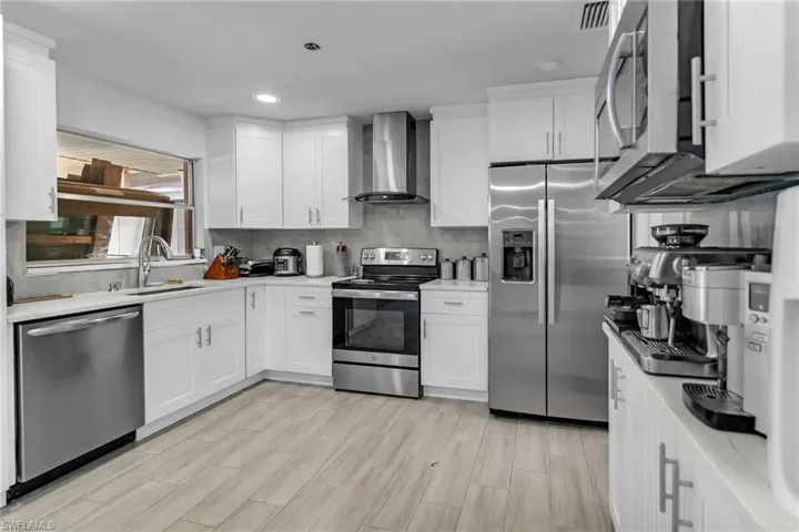 Kitchen with white cabinetry, stainless steel appliances, wall chimney range hood, and light hardwood / wood-style floors
