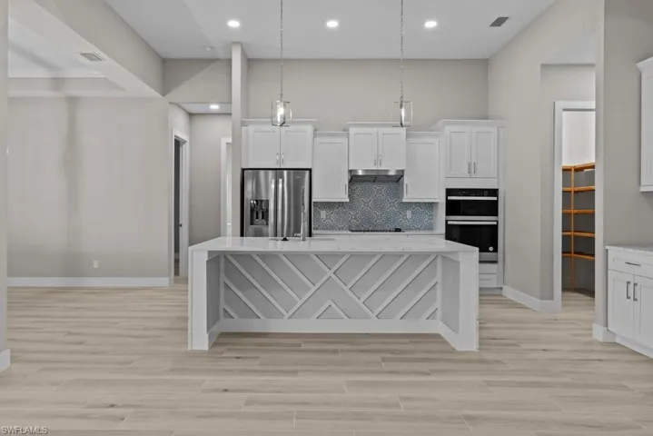 Kitchen with stainless steel refrigerator with ice dispenser, double oven, a center island with sink, white cabinetry, and light wood-style flooring