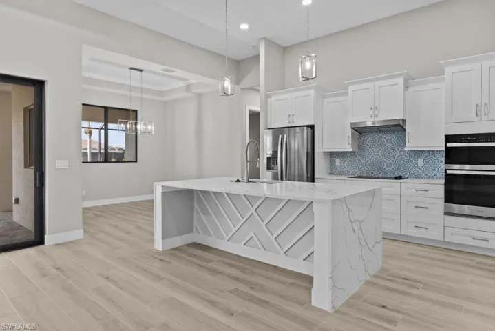 Kitchen with stainless steel appliances, a sink, decorative backsplash, a center island with sink, and white cabinetry