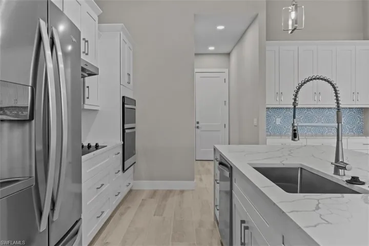 Kitchen with appliances with stainless steel finishes, a sink, white cabinets, under cabinet range hood, and recessed lighting