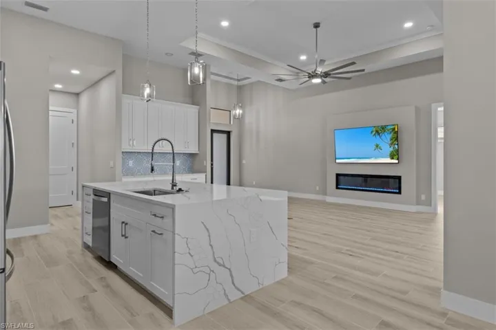 Kitchen featuring stainless steel dishwasher, a sink, white cabinets, light stone countertops, and a center island with sink