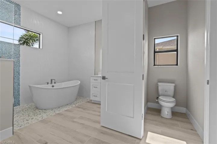 Bathroom with healthy amount of natural light, a freestanding bath, toilet, wood finished floors, and recessed lighting