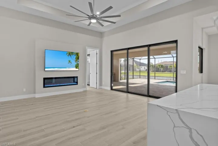 Living area with ceiling fan, light wood finished floors, baseboards, a glass covered fireplace, and ornamental molding