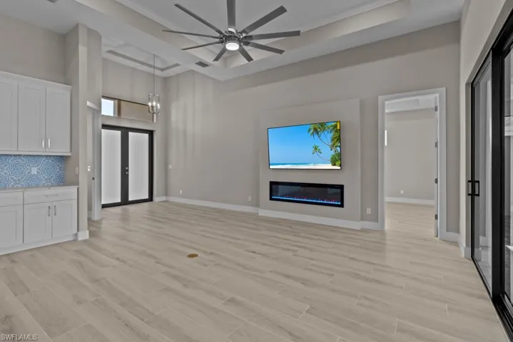 Unfurnished living room featuring a ceiling fan, a glass covered fireplace, light wood-style flooring, baseboards, and a towering ceiling