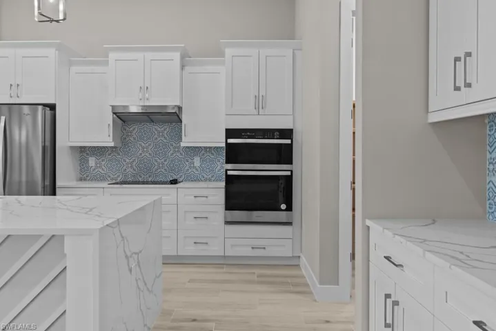 Kitchen with under cabinet range hood, backsplash, white cabinetry, and black electric stovetop