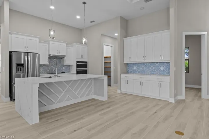 Kitchen featuring stainless steel refrigerator with ice dispenser, a towering ceiling, backsplash, white cabinets, and an island with sink
