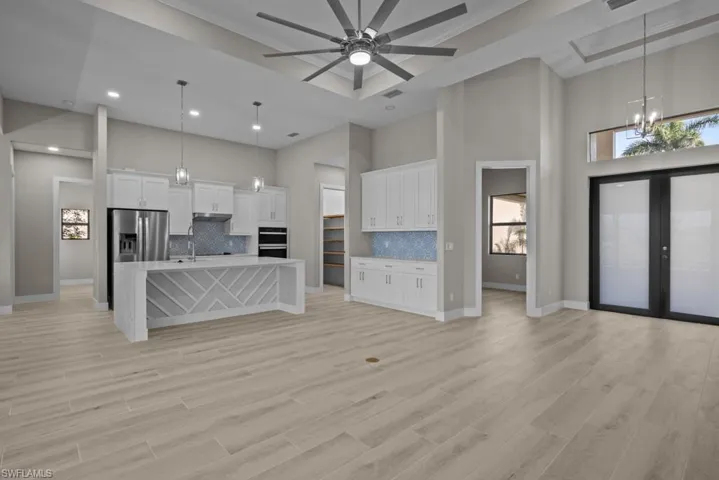 Unfurnished living room featuring a high ceiling, a chandelier, a ceiling fan, recessed lighting, and baseboards