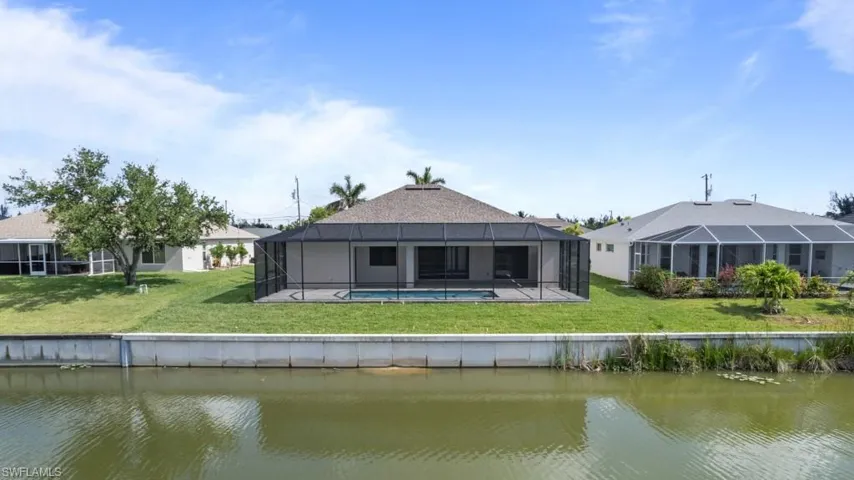Back of house with a water view, a yard, glass enclosure, and an outdoor pool