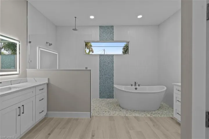 Full bath with a walk in shower, vanity, wood finished floors, a soaking tub, and recessed lighting