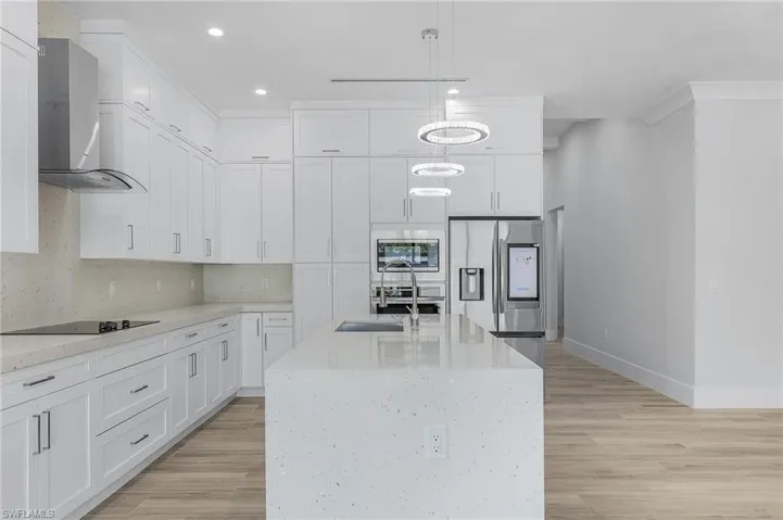 Kitchen with light stone countertops, light wood finished floors, stainless steel appliances, and white cabinets