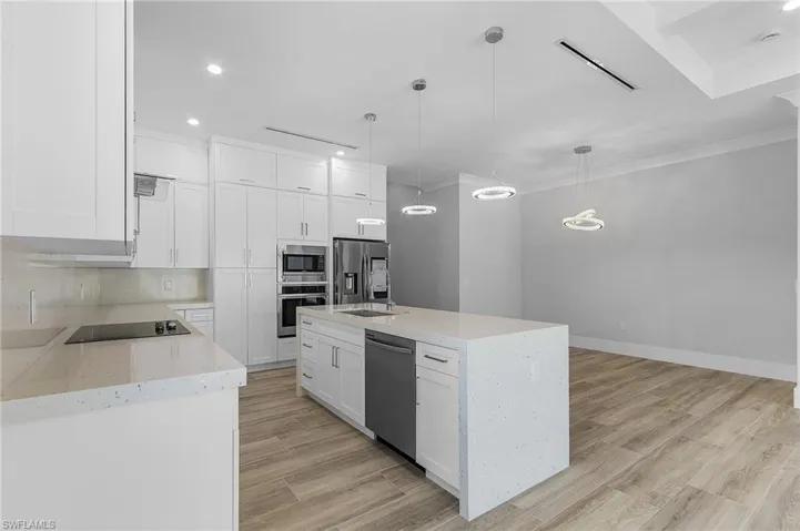 Kitchen with light stone countertops, white cabinets, light wood-style flooring, decorative light fixtures, and stainless steel appliances