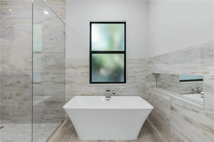 Bathroom featuring a soaking tub, tile walls, a marble finish shower, and wainscoting