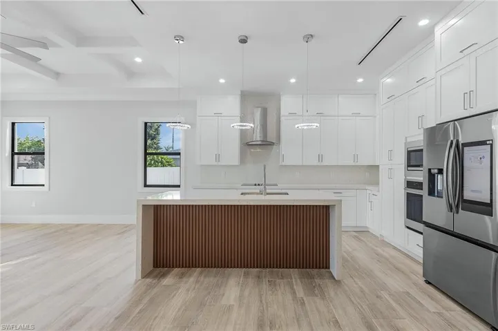 Kitchen featuring stainless steel appliances, light stone counters, beam ceiling, an island with sink, and decorative light fixtures