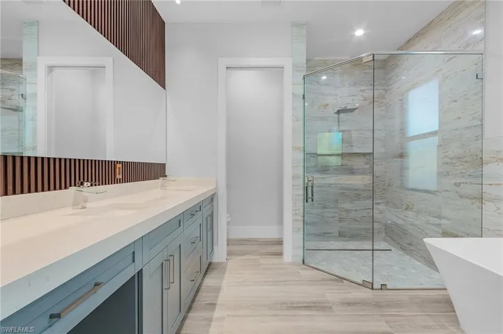 Bathroom with double vanity, a marble finish shower, and a soaking tub