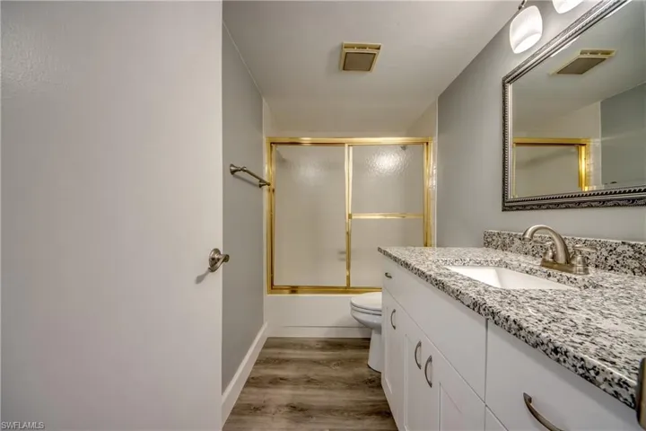 Bathroom featuring vanity, shower / bath combination with glass door, and light wood-type flooring
