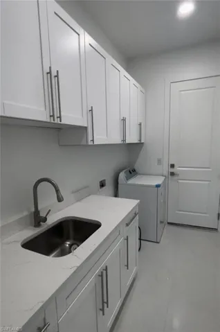 Laundry area with light tile patterned floors, sink, and cabinets