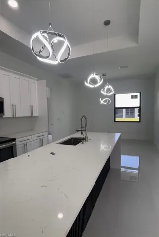 Kitchen with a raised ceiling, tile patterned flooring, light stone counters, sink, and decorative light fixtures