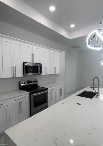 Kitchen featuring appliances with stainless steel finishes, white cabinetry, sink, and light stone countertops