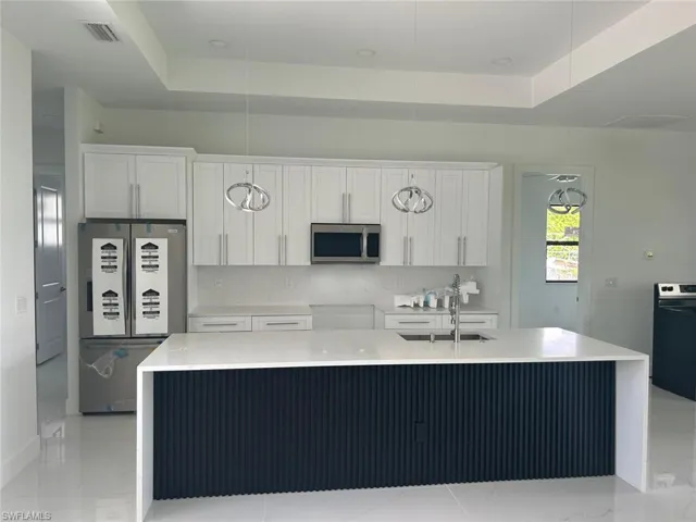 Kitchen with a kitchen island with sink, sink, a tray ceiling, and stainless steel appliances