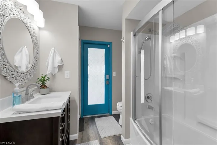 Full bath with vanity, shower / bath combination with glass door, and dark wood-type flooring