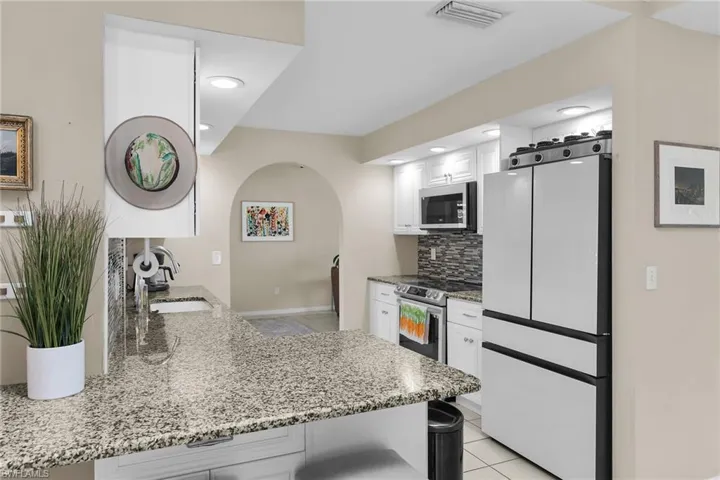 Kitchen with stainless steel appliances, light stone counters, a peninsula, white cabinetry, and a kitchen bar