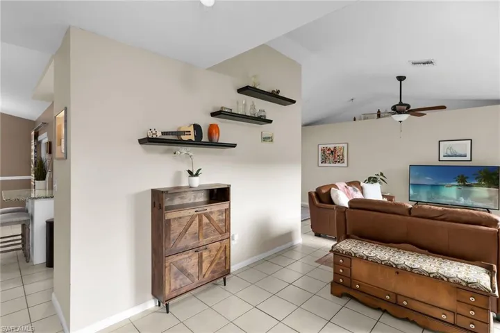 Living room with lofted ceiling, a ceiling fan, and light tile patterned flooring
